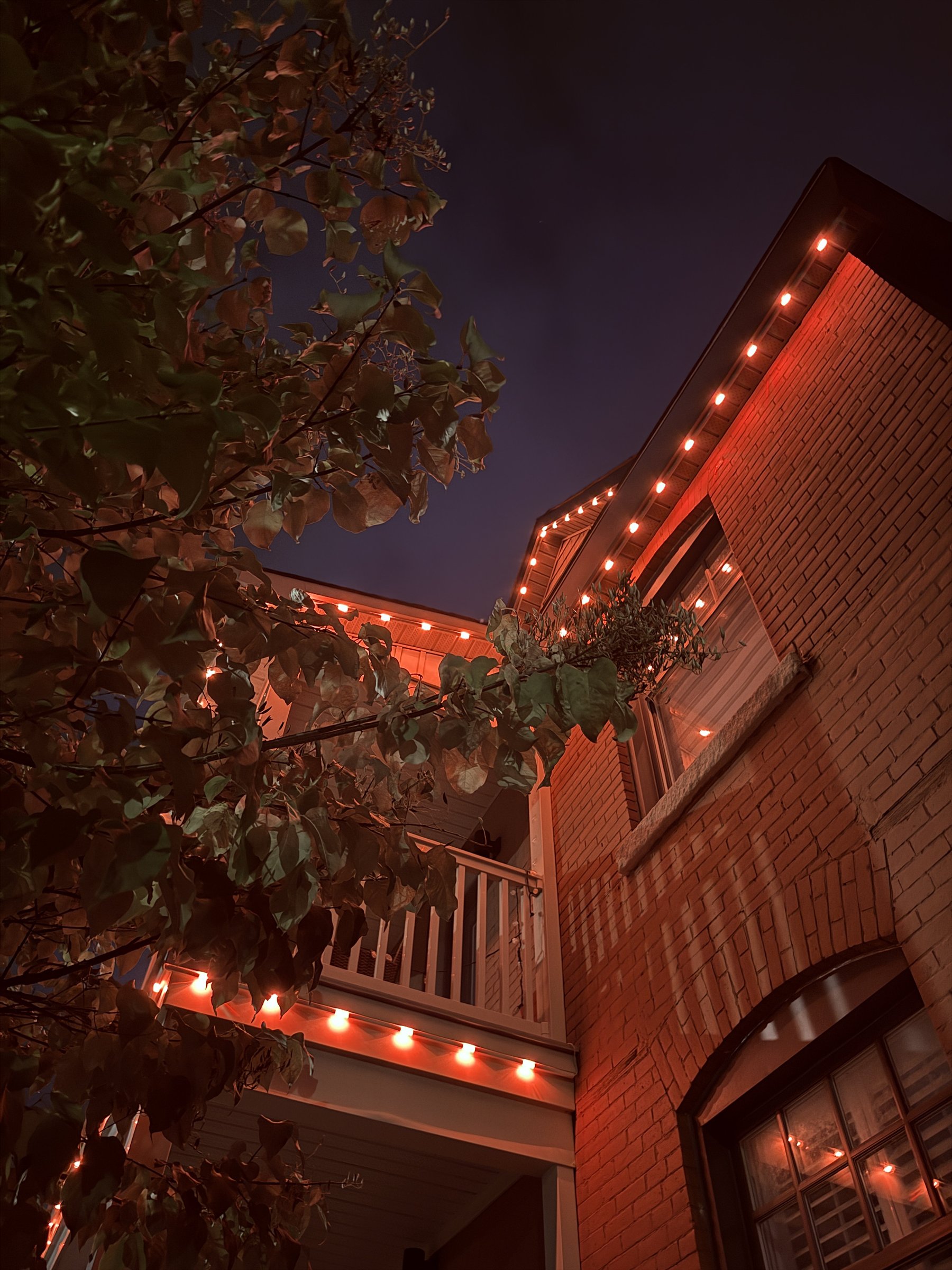 Red permanent lights viewed through the architecture and trees of an Ottawa-area home
