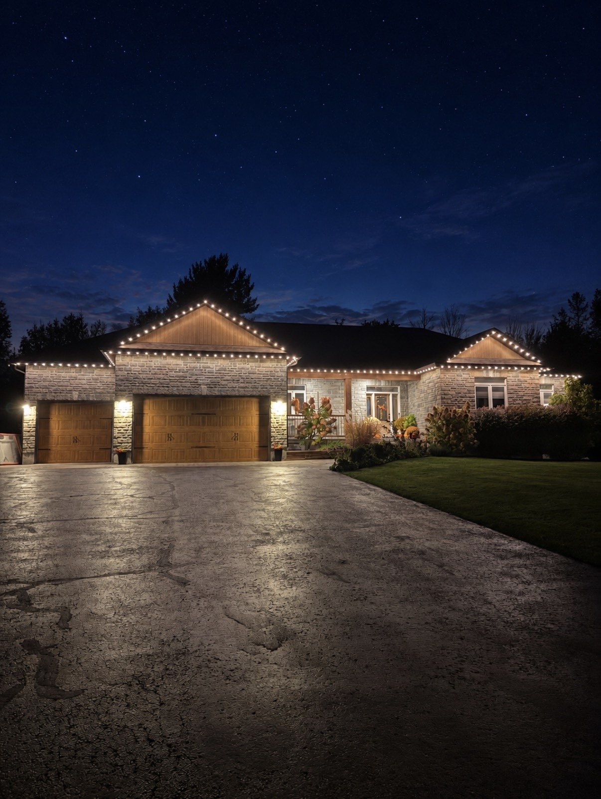 Warm white permanent roofline lighting on an Ottawa-area stone home beneath a starry sky