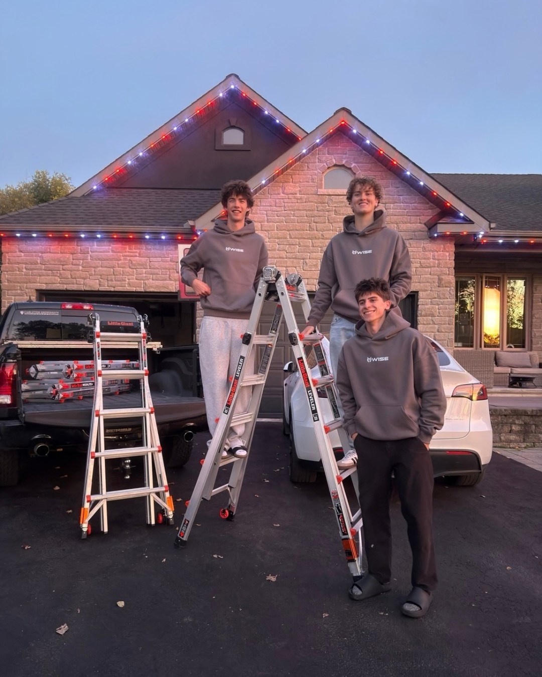 Three Wise Outdoor Lighting crew members with installation ladders in front of a completed red and white roofline project